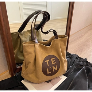 Detail view of khaki canvas tote bag with brown leather handles and TELN logo patch