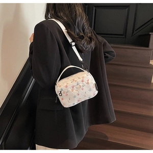 Close-up of floral embroidery on a white crossbody bag with adjustable strap and dark suit
