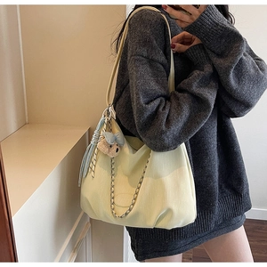 Close-up of beige tote bag with soft leather texture, chain detail, and plush bear charm