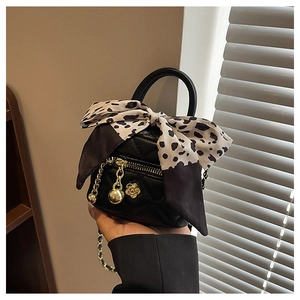 Detail of black quilted mini bag with polka dot bow and golden floral charms