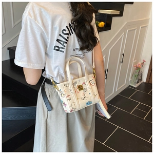 Detail of a white bucket bag with colorful graffiti patterns and gold hardware on model