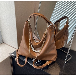 Detail shot of brown hobo bag featuring pearl and gold chain charms on soft leather