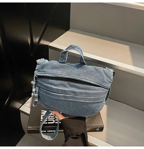 Close-up of a blue denim crossbody bag featuring a curved design and raw fringe edges