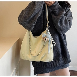 Detail view of cream hobo tote bag with silver chain strap and plush bear accessory