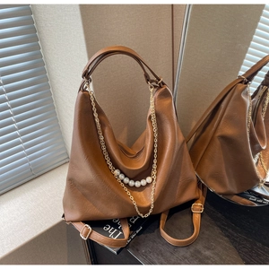 Detail of a brown leather tote bag with gold chain and pearl charm against a mirror backdrop