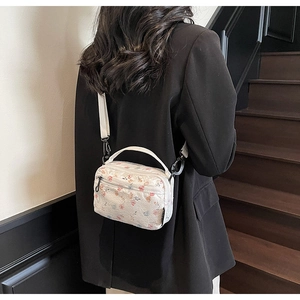 Floral print crossbody bag with white shoulder strap shown on a black suit blazer