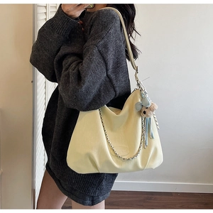 Detail of cream tote bag with metal chain and plush bear charm worn by a model