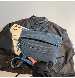 Detail of blue denim backpack showing top handle and front zipper pocket on leather background