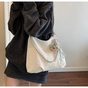 Detailed macro view of white textured tote bag with chain strap and teddy bear charm