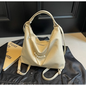 Detail of cream hobo bag with gold chains and large pearls on a black leather jacket