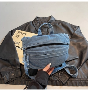 Detail of blue denim crossbody bag featuring washed texture and sturdy black zipper design
