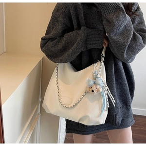Detail of white hobo bag with vertical quilting, chain strap, and plush bear charm