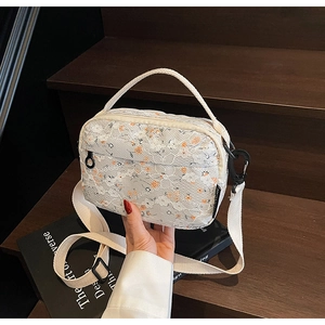 Detail of white lace floral crossbody bag featuring embroidered orange flowers and strap