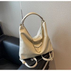 Detail of cream hobo bag with gold chain and white pearls on a black leather sofa