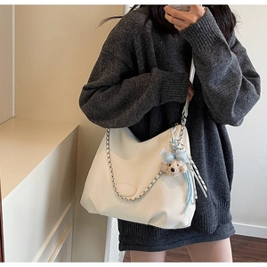 Detail of off-white textured tote bag with silver chain strap and plush bear charm