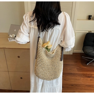 Detailed view of woven straw tote bag with brown leather strap in a home setting