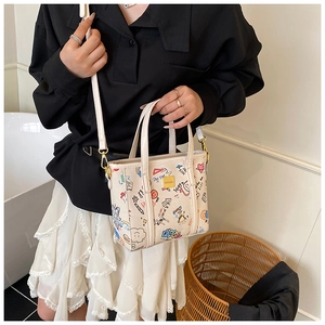 Detail showing cream-colored mini tote bag with colorful hand-drawn graffiti and gold hardware
