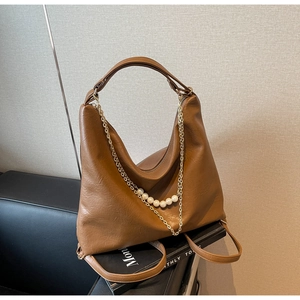 Detail of a brown leather hobo bag with a decorative metal chain and pearl ornament