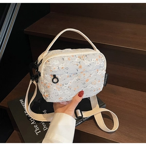 Close-up of white floral lace shoulder bag with woven strap and brand label detail