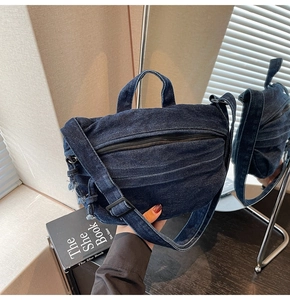Detail of blue denim shoulder bag showing frayed edges and adjustable wide strap