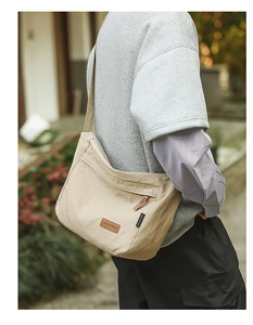 Detail of water-resistant beige nylon messenger bag with leather logo patch and zip pocket