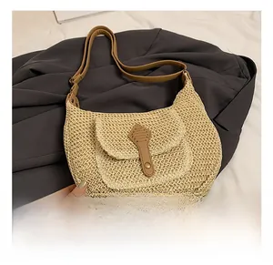 Detailed straw woven texture of beige crescent bag with brown leather front pocket and metal snap