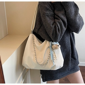Close-up of minimalist off-white leather tote bag with silver chain and cute teddy bear charm