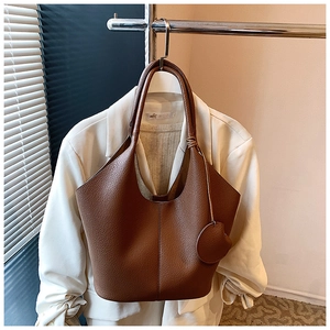 Brown lychee grain leather tote bag with stitch detail hanging by white suit jacket