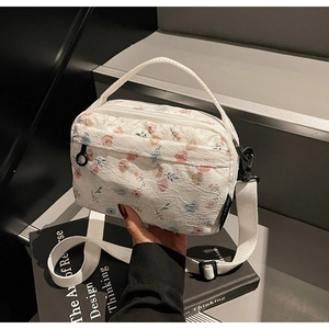 Detail of white lace square bag featuring colorful floral patterns and wide strap