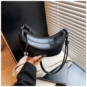 Gros plan du sac demi-lune en cuir noir souple avec bandoulière à nœud et logo argenté
