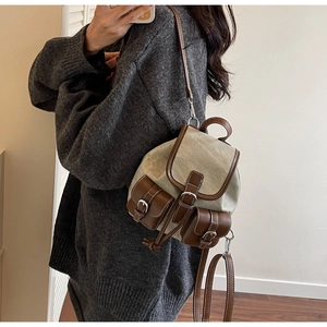 Detail of a vintage beige canvas mini backpack with brown leather trim worn by a model