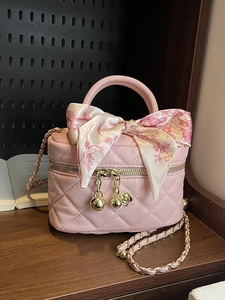 Pink quilted mini crossbody bag with gold ball chain and silk ribbon on wood table