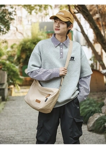 Close-up of large khaki nylon messenger bag with adjustable strap in outdoor street setting