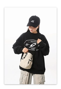 Sac bandoulière imperméable beige sable porté avec un sweat à capuche noir imprimé