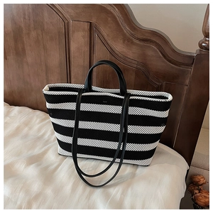 Détail du cabas en tricot à rayures avec poignées en cuir noir sur un fond de lit minimaliste