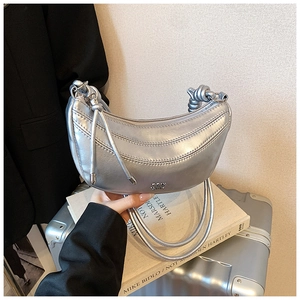 Détail du sac demi-lune argenté avec matelassage et logo métallique sur un livre d'art