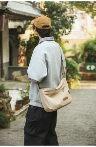 Close-up of durable beige nylon messenger bag featuring a brown leather logo patch and zip pocket