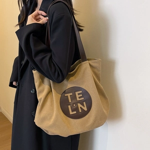 Large canvas tote bag with leather trim and brown straps, shown on model with black coat