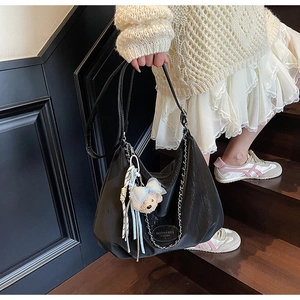 Detail of black leather hobo bag with metal chain and cute plush bear accessory