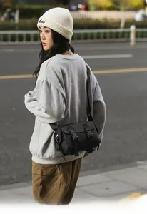 Street style shot of a black matte messenger bag with buckle straps and side woven label