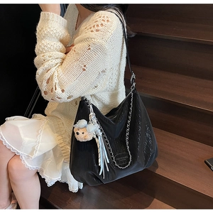 Detail of black leather tote bag with silver chain, logo tag and plush bear charm decoration