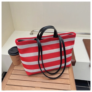 Détail du sac cabas en mesh rayé rouge et blanc avec double poignées en cuir sur banc