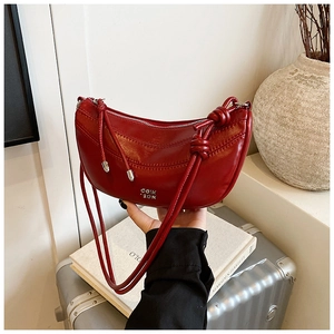 Détail du sac demi-lune rouge au fini brillant avec bandoulière à nœud décoratif