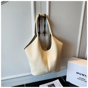 Detail view of beige lychee textured leather tote bag hanging on white wooden cabinet