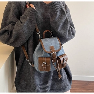 Detail of vintage canvas backpack with brown leather trim and metal buckles worn by model