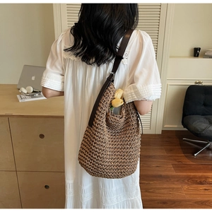 Detail view of woven straw tote bag with brown leather strap and side pocket detail