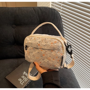 Close-up of white floral lace crossbody bag with canvas handle and black hardware
