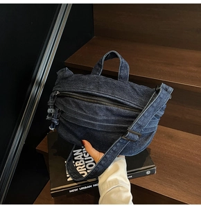 Detail of a dark blue denim crossbody bag placed on wooden steps with vintage books