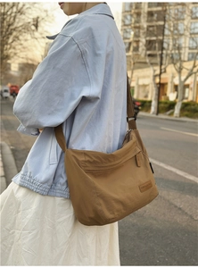 Brown canvas messenger bag with adjustable strap and logo detail in urban street setting