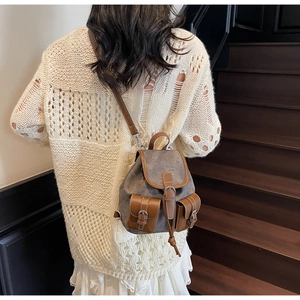 Close-up of retro plaid canvas mini backpack with brown leather trim on beige sweater